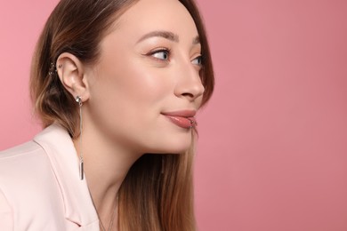 Young woman with lip and ear piercings on pink background, space for text