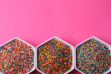 Colorful sprinkles in bowls on pink background, flat lay with space for text. Confectionery decor