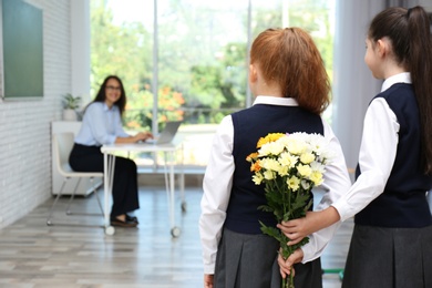 Schoolgirls with bouquet congratulating their pedagogue in classroom. Teacher's day