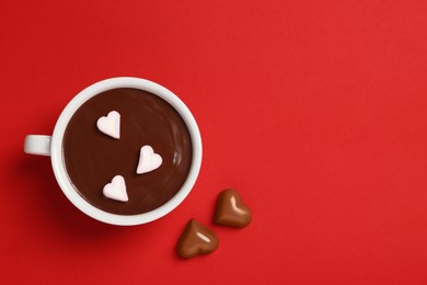 Photo of Cup of hot chocolate with heart shaped marshmallows and tasty candies on red background, flat lay. Space for text
