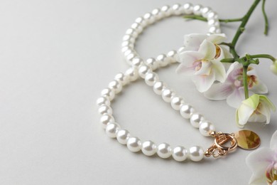 Photo of Elegant pearl necklace and orchid flowers on white background, closeup