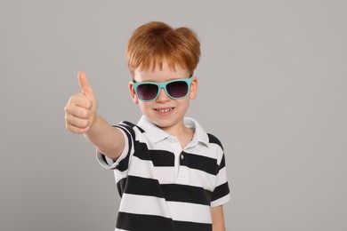 Cute little boy with sunglasses on light grey background