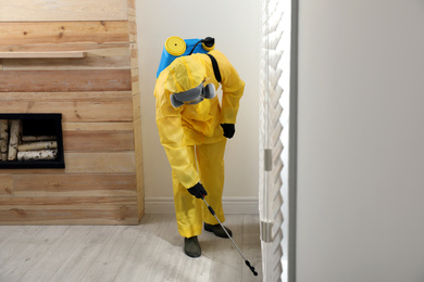Pest control worker in protective suit spraying insecticide on floor at home