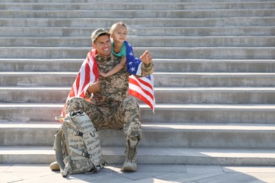 Soldier with flag of USA and his little daughter outdoors, space for text