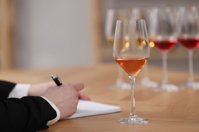 Sommelier making notes during wine tasting at table indoors, closeup
