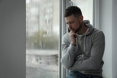 Depressed man near window at home. Space for text