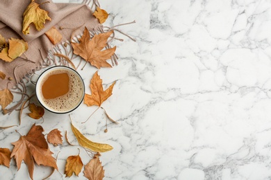Flat lay composition with cup of hot drink, scarf and autumn leaves on white marble background, space for text. Cozy atmosphere
