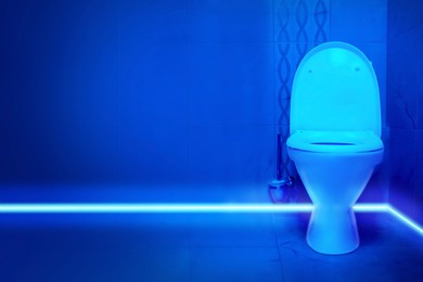 Toilet bowl in public restroom lit with UV blue light