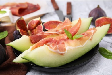 Tasty melon, jamon and figs served on white textured table, closeup