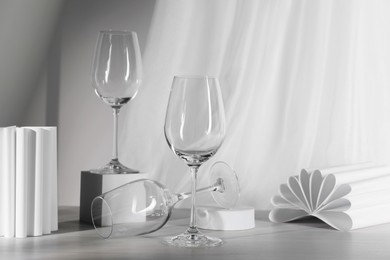 Photo of Empty wine glasses, folded paper decor and cube on white wooden table