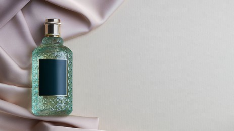 Photo of Bottle of luxurious perfume and beige silk fabric on light background, top view. Space for text