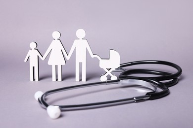 Photo of Figures of family stainding near stethoscope on lilac background. Insurance concept