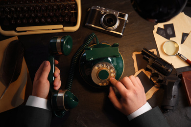 Detective dialing number on vintage telephone at table, top view