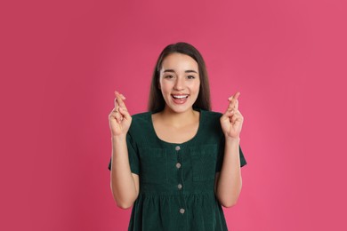 Woman with crossed fingers on pink background. Superstition concept