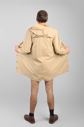 Exhibitionist exposing naked body under coat on light background, back view