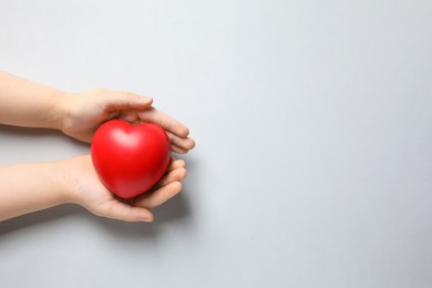 Photo of Child holding red heart on light grey background, top view. Space for text
