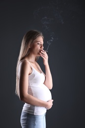 Young pregnant woman smoking cigarette on dark background. Harm to unborn baby