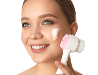 Young woman washing face with brush and cleansing foam on white background. Cosmetic products