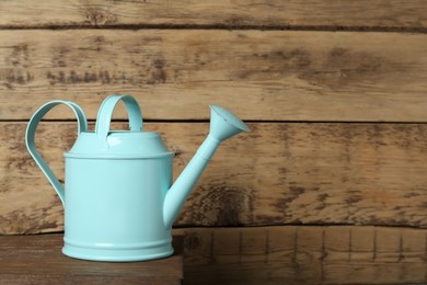 Photo of Turquoise metal watering can on table against wooden background, space for text