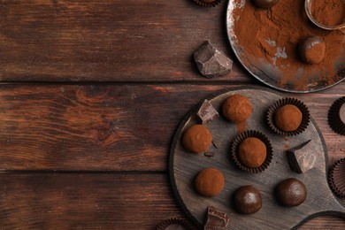 Delicious chocolate truffles powdered with cocoa on wooden table, flat lay. Space for text