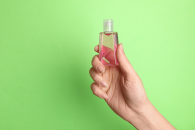 Photo of Woman holding antiseptic gel on green background, closeup