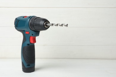 Modern electric power drill on white wooden table, space for text