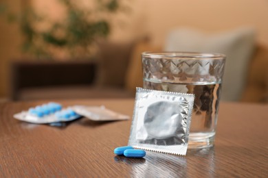 Photo of Glass of water, condoms and pills on wooden table indoors, space for text. Potency problem concept