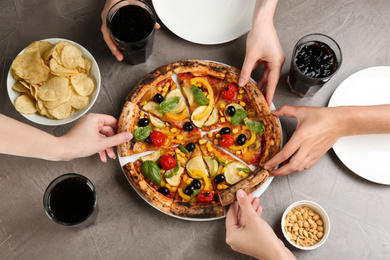Photo of Women taking slices of delicious vegetable pizza at grey table, closeup