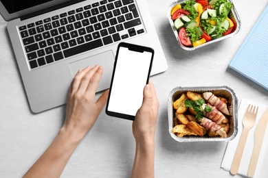 Top view of woman holding smartphone over white wooden table with lunchboxes,  mockup for design. Healthy food delivery