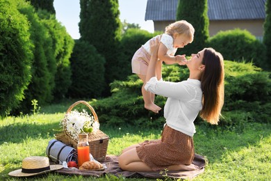 Mother and her baby daughter playing while having picnic in garden on sunny day
