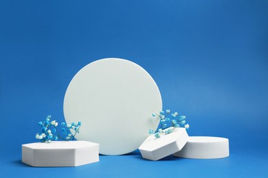 Photo of Product photography props. Podiums of different geometric shapes and flowers on blue background