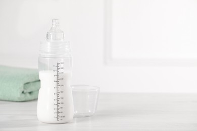 Photo of Feeding bottle with milk on white wooden table. Space for text