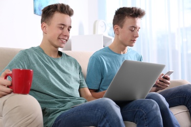 Teenage twin brothers together on sofa in living room