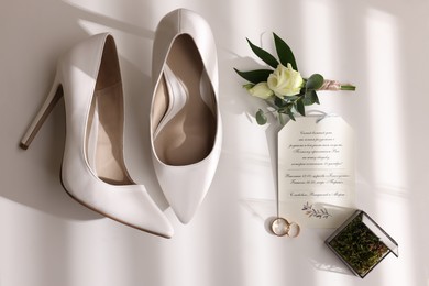 Beautiful bride's shoes, wedding rings, glass box, boutonniere and invitation on white background, top view