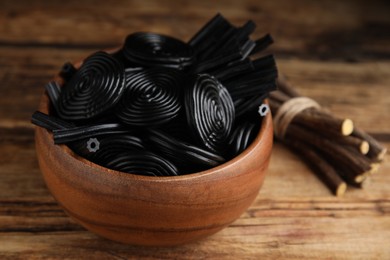 Tasty black candies and dried sticks of liquorice root on wooden table, closeup