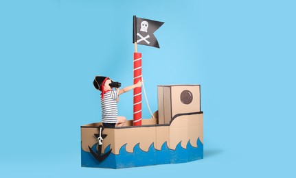 Photo of Little boy playing with binoculars in pirate cardboard ship on turquoise background