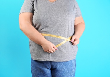 Photo of Overweight woman measuring waist before weight loss on color background