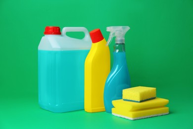Different cleaning supplies and sponges on green background