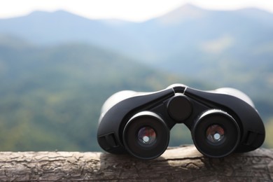 Modern binoculars on wooden log in mountains, space for text