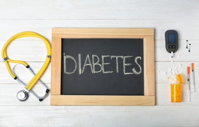 Flat lay composition with word "Diabetes", digital glucometer, stethoscope and medicine on wooden background