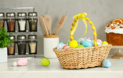 Photo of Easter basket with tasty painted eggs near cake on white countertop in kitchen