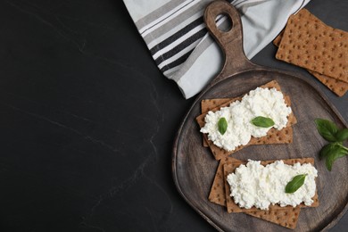 Photo of Crispy crackers with cottage cheese and basil on black table, flat lay. Space for text