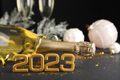 Happy New Year 2023! Bottle of sparkling wine and festive decor on table against black background