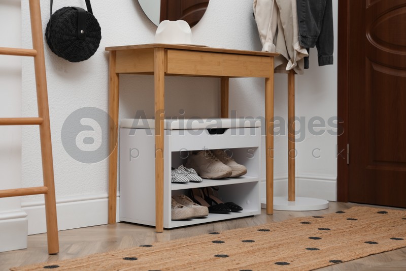 Shelving unit with shoes and accessories near white wall in hall