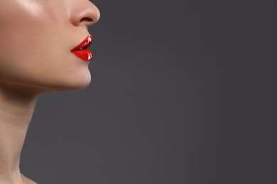 Photo of Young woman with beautiful red lips on grey background, closeup. Space for text