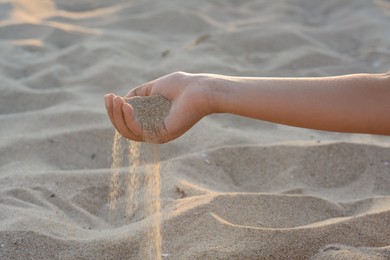 Girl pouring sand from hand outdoors, closeup. Fleeting time concept