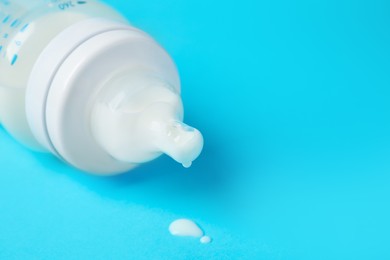 Photo of One feeding bottle with milk on light blue background, closeup. Space for text