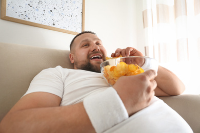 Lazy overweight man eating chips at home