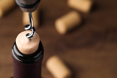 Photo of Opening wine bottle with corkscrew on wooden table, closeup. Space for text