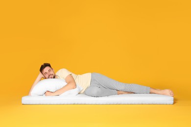 Photo of Smiling man lying on soft mattress against orange background